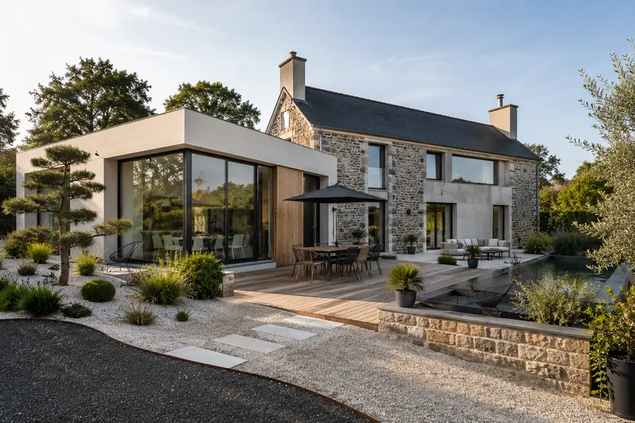Maison en pierre prolongée par un volume contemporain enduit blanc à grandes baies, terrasse en bois et jardin minéral.